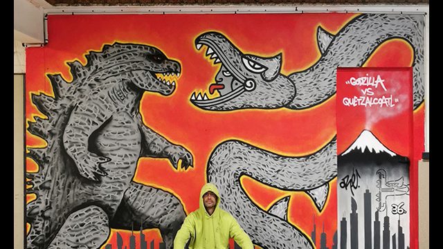 Fresque de l'artiste graffeur Oré. Godzilla et Quetzalcóatl sont face à face sur un fond rouge et orange. Cette œuvre de street art est en Normandie.