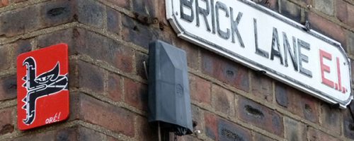 Œuvre street art de l'artiste graffeur Oré. Serpent à plumes, Quetzalcóatl, collé à Londres. Avec le panneau de rue Brick Lane.