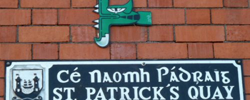 Œuvre street art de l'artiste graffeur Oré. Serpent à plumes, Quetzalcóatl, collé dans les rues de Cork en Irlande. Couleur verte sur un mur de brique rouge.