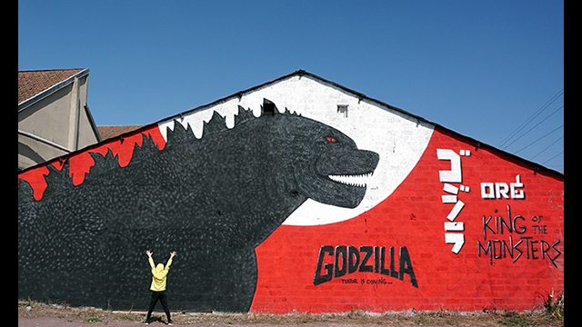Fresque street art de l'artiste graffeur Oré. Godzilla géant sur fond rouge.