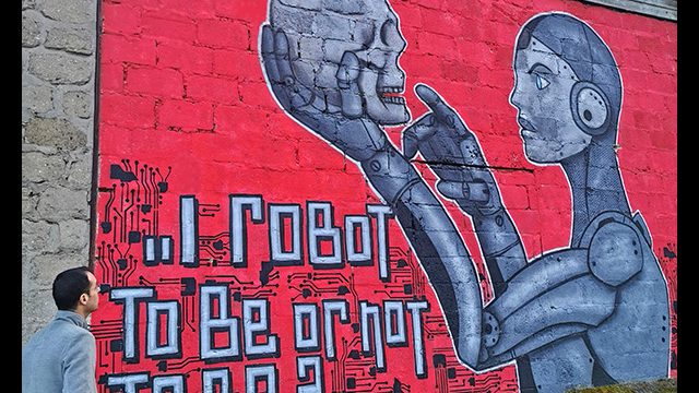 Fresque de l'artiste graffeur Oré. Cette œuvre de street art représente un robot regardant un crâne humain. Couleur rouge en fond et ton gris pour le robot.