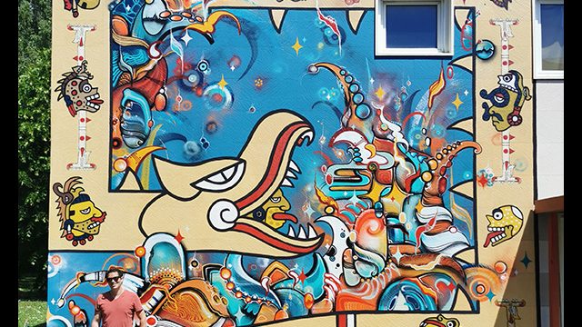 Fresque sur une façade extérieure peinte par le graffeur et street artiste Oré. Un Quetzalcóatl géant de couleur crème serpente sur un fond abstrait bleu.