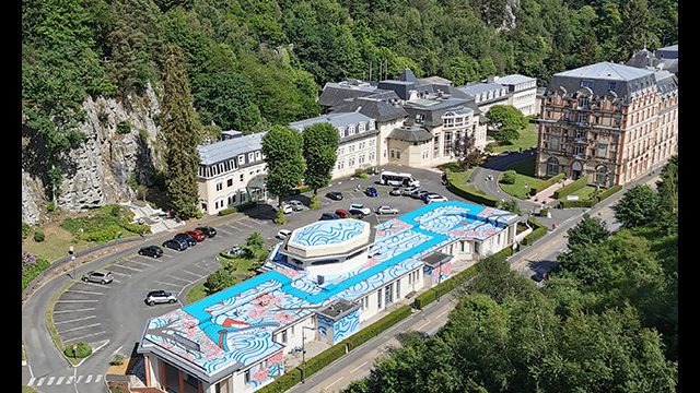 Fresque de l'artiste graffeur Oré sur le toit de la station thermale à Bagnoles-de-l'Orne. Vue large. Street Art XXL.