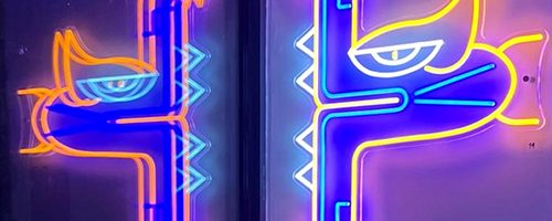 Tête de Serpent à plumes en néon lumineux dans la nuit. Couleurs bleu, orange et bleu. Oeuvre du street artiste Oré.