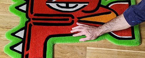 Tapis de l'artiste graffeur Oré. Tête de Quetzalcóatl en laine. Couleurs rouge, vert et blanc.